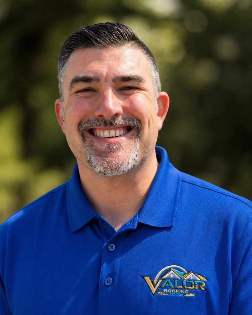 Smiling man with short dark hair and gray beard wearing a blue polo shirt with the Valor Roofing logo, outdoors.
